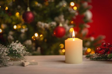 Ahşap bir masada parlayan ılık bir Noel mumu festival ışıkları ve süsleri mevsimlik temalar için arka planda yavaşça bulanıklaşıyor.