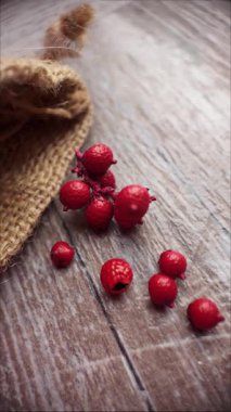 Kamera kırsal ahşap yüzeyde sola hareket ederken çuval bezinden dökülen kırmızı böğürtlenlerin dikey yavaş çekim makro klipsi.