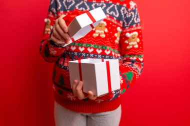 Çocuk kırmızı arka planda kırmızı kurdeleli beyaz bir hediye kutusu açıyor. Bayram reklamları, tatil mesajları ve mevsimlik markalar için ideal.