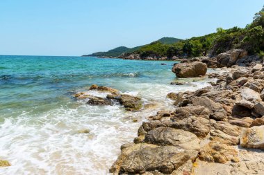 Olympiada, Yunanistan 24 Temmuz 2021: Olimpiyat yakınlarındaki Babylon Plajı 'nda kayalara vuran dalgalar, açık mavi deniz ve yaz boyunca yeşil tepeler.