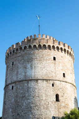 Selanik 'in Beyaz Kulesi, açık mavi gökyüzüne karşı, dairesel taş yapısını, siperlerini ve tarihsel savunma mimarisini vurguluyor.