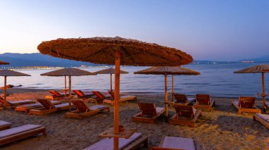 Plaj şezlongları ve saman şemsiyeleri sıcak akşam ışıklarıyla aydınlatılarak gün batımından sonra rahat bir deniz havası yaratılıyor.