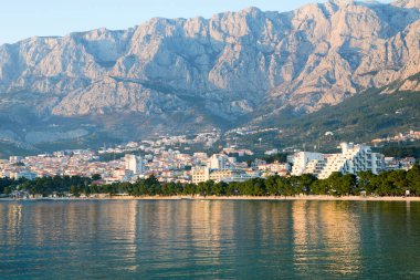 Makarska, Hırvatistan, 31 Mart. Sakin Adriyatik Denizi ile Makarska sahilinin 2019 Panoramik manzarası şehrin ufuk çizgisini ve Biokovo sıradağlarını yansıtıyor