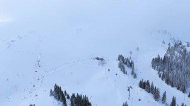 Gondol istasyonları ve kayakçılarla sisli kayak merkezinin hava manzarası, kış hava koşullarını ve dağlık dağ atmosferini gösteriyor
