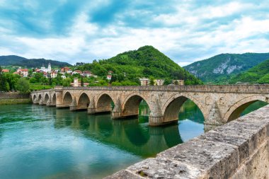 Bosna-Hersek 'in Višegrad kentindeki İkoniç Osmanlı taş köprüsü, Drina Nehri' ni kemerlerle geçerek temiz yeşil suya yansıyor.