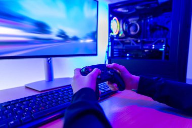 Yüksek hızlı yarış oyunu sırasında kontrolörü elinde tutan oyuncu, güçlü oyun bilgisayarının yanında monitörde görüntülenen hareket bulanıklığı görüntülerine odaklanmış.