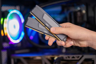 Oyun bilgisayarının önünde iki DDR5 bellek modülü, RGB ışıklandırması, yüksek performans sistemi güncellemesi.