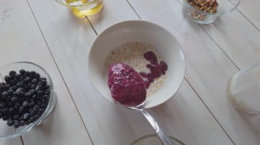 Yavaş çekimde yaban mersinini sütlü yulaf ezmesi kasesine eklemek, sağlıklı antioksidan kahvaltı hazırlamak.