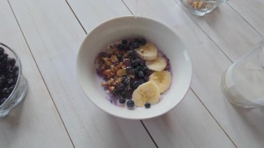 Meyve ve fındıklı yulaf ezmesi üzerine serpiştirilmiş altın bal, yavaş çekim sağlıklı kahvaltı hazırlığı.