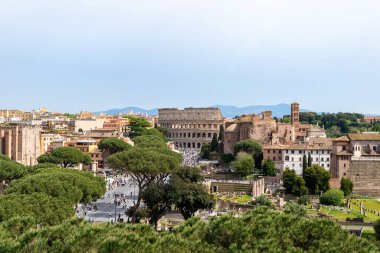 Roma, İtalya 20 Nisan 2025 Kolezyum 'un panoramik manzarası ve Ebedi Şehrin tarihi kalbindeki ağaçlar tarafından çerçevelenmiş antik kalıntılar.