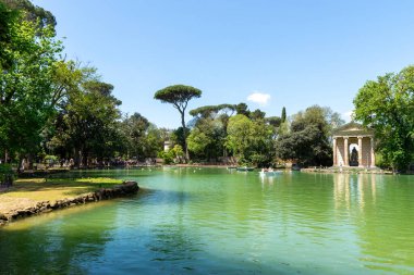 Roma, İtalya 22 Nisan 2025 Villa Borghese Parkı 'nda açık mavi gökyüzünün altında, yemyeşil ve klasik mimari ile çevrili tekneler süzülüyor.