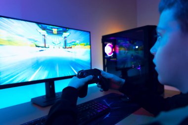 Masaüstü oyun bilgisayarında neon mavi ve mor LED ışık ayarlı kontrolörle yarış oyunu oynayan genç çocuk.