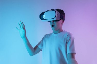Sanal gerçeklik kulaklığı takan genç çocuk, gelecekteki teknolojiye duygusal tepki kavramı olan dijital ortama tepki verirken şaşırmış veya endişeli ifadeyle el kaldırıyor.