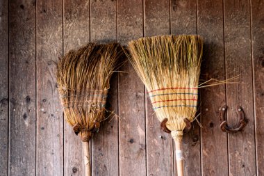 İki süpürge, ahır panelindeki paslı at nallarından yapılmış bir süspansiyon.