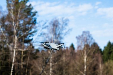 Gökyüzünde uçan dron, yan görüş, arka planda ağaçlar