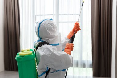 Yatak odasındaki evi dezenfekte eden koruyucu giysili bir adam, bulaşıcı Corona virüsü yaymayı bırak..