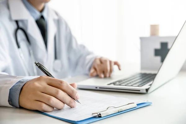 Doctor writing on document file while he use computer in his office