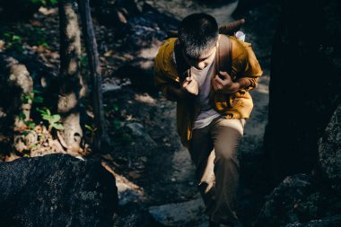 Asyalı genç dağların zirvesine tırmanmak için ormanda yürüyüş yapıyor..