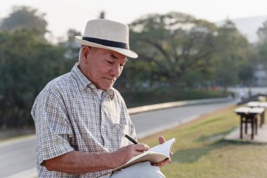 Asyalı yaşlı adam halka açık parkta oturuyor ve dinleniyor..