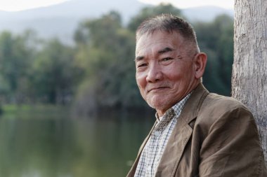 Asyalı yaşlı adam halka açık parkta oturuyor ve dinleniyor..