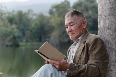 Asyalı yaşlı adam halka açık parkta oturuyor ve dinleniyor..