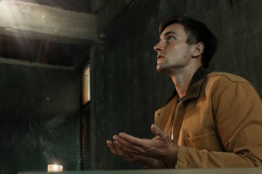 Yalnız başına mum ve İncil 'le dua eden adam.