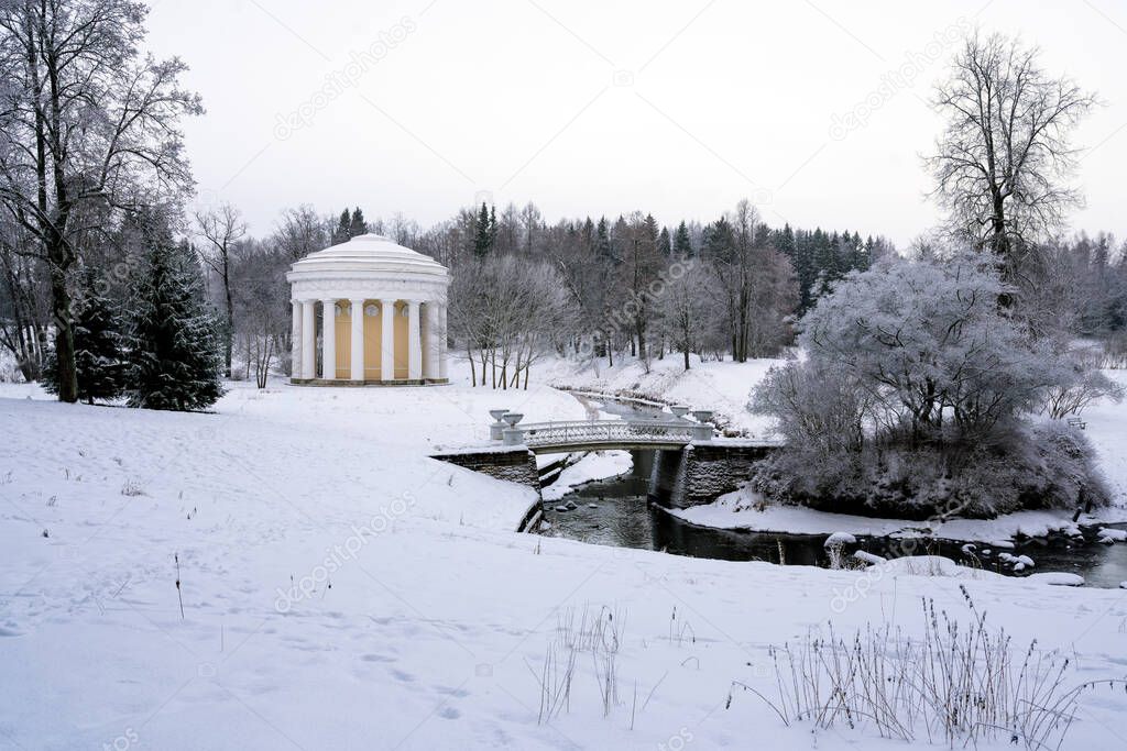 View of the Cast-iron bridge over the Slavyanka River and the Temple of Friendship in the Pavlovsk Palace and Park Complex on a winter cloudy day, St. Petersburg, Russia