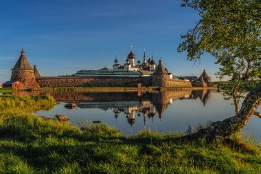 Solovetsky Manastırı 'nı kutsal gölün yanından güneşli bulutsuz bir sabahta kıvrımlı bir kuzey huş ağacının arka planında, Solovetsky Adası, Arkhangelsk Bölgesi, Rusya
