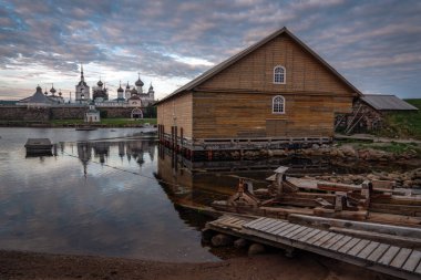 Beyaz Deniz Koyu 'nun kıyısındaki teçhizat ambarı ve arka planda Spaso-Preobrazhensky Solovetsky Manastırı bulutlu günbatımına karşı Solovetsky Adası, Arkhangelsk bölgesi.