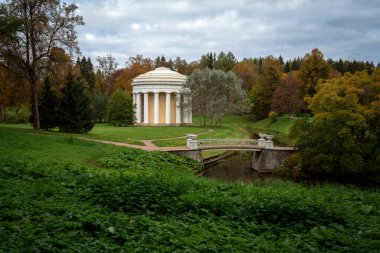 Slavyanka Nehri üzerindeki dökme demir köprü ve Pavlovsk Sarayı ve Park Kompleksi 'ndeki Dostluk Tapınağı, sonbahar bulutlu bir sabahta, St. Petersburg, Rusya