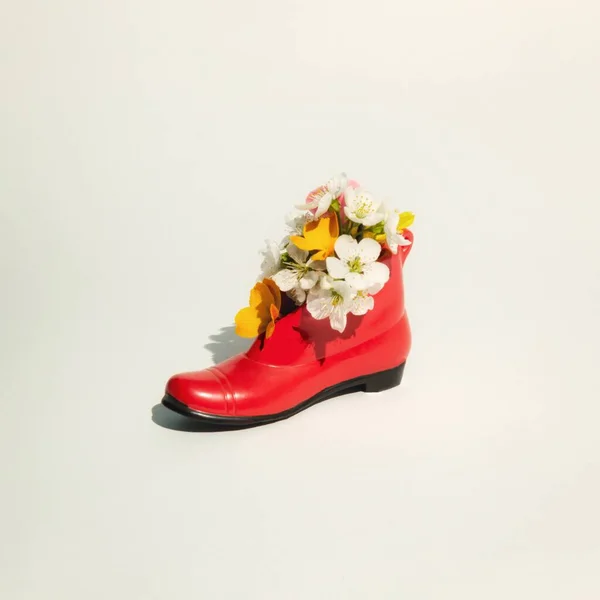 Minimal fashion concept with red shoe and spring colorful flowers on bright background. Environmental protection and sustainability idea.