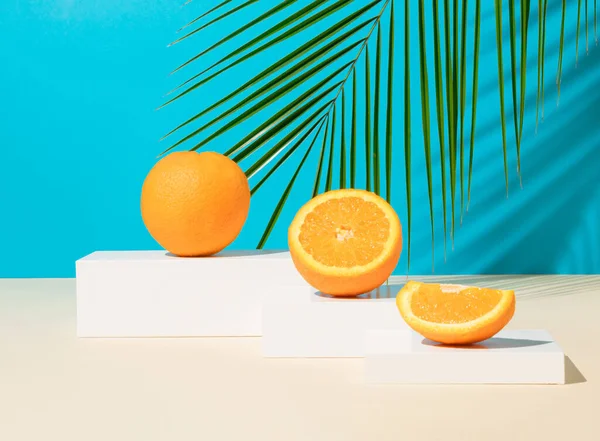 Podyumda taze ve olgun portakal meyveli modern hayat ya da tropikal palmiye yaprağıyla mavi arka planda kaide. Minimum detoks diyeti veya yaz konsepti.