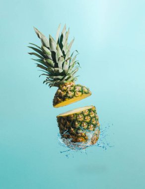 Pastel mavi arka planda su sıçraması olan dilimlenmiş ananas. Minimum meyve konsepti. Yaz tropik fikri.