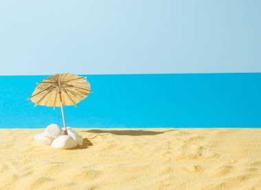 Mavi arkaplanda kumdaki güneş şemsiyesi. Yaratıcı sahil tatili konsepti. Asgari yaz fikri.