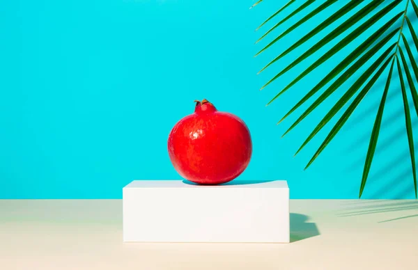 简约的夏季作曲 石榴果立在白色的基座上 棕榈枝在蓝色的背景下 具有复制空间的创新热带或食品概念 — 图库照片