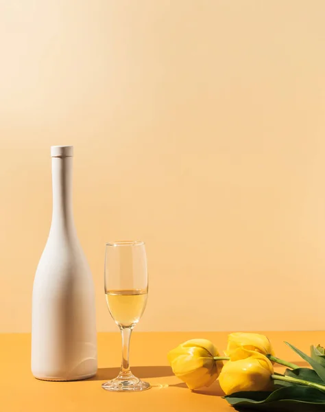 オレンジの背景に影のある白ワインボトルとガラス エレガントなお祝いの組成 テーブルの上にチューリップの花 パーティーのコンセプト — ストック写真