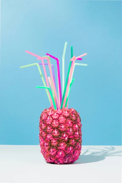Pink pineapple with colorful cocktail straws on sky blue background. Creative food composition. Party minimal concept.