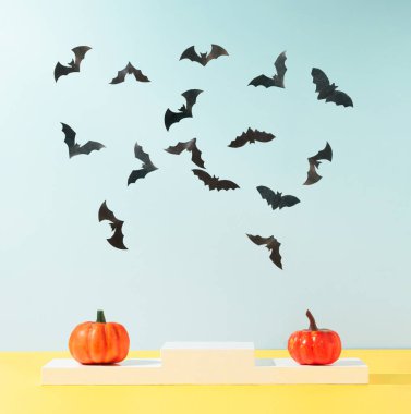 Gökyüzü mavisi arka planda podyum renkli sonbahar balkabakları ve yarasaların siluetleriyle modern ürün sergileniyor. Ürün Gösterimi ve İş Konsepti için uygundur. Moda Cadılar Bayramı geçmişi.