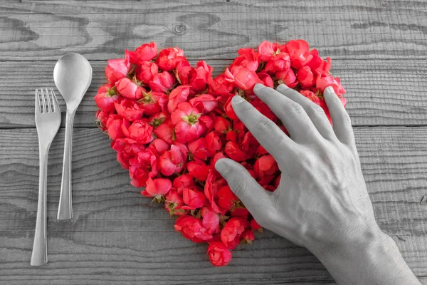 Cuore fatto di rose rosse su sfondo di legno, coperto da una mano — Foto Stock