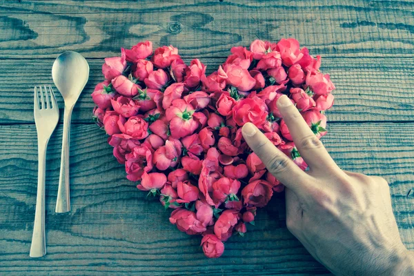 Corazón hecho de rosas rojas en fondo de madera, cubierto por una mano — Foto de Stock
