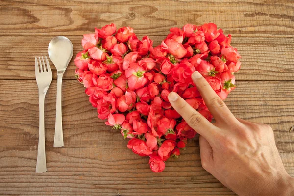 Coeur en roses rouges en fond de bois, recouvert d'une main Photo De Stock