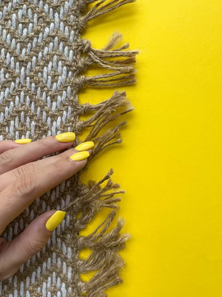 Sarı arka planda sarı manikürlü bir kız eli. El yapımı halı..