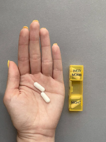 Sarı organizatör ve gri arka planda hapları olan bir kadın eli..