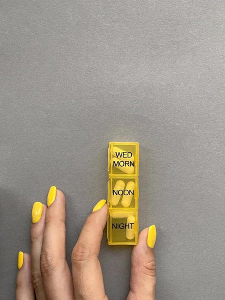 Kızın elinde sarı bir hap kutusu var..