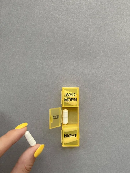 Elinde haplar ve gri arka planda sarı bir hap organizatörü..