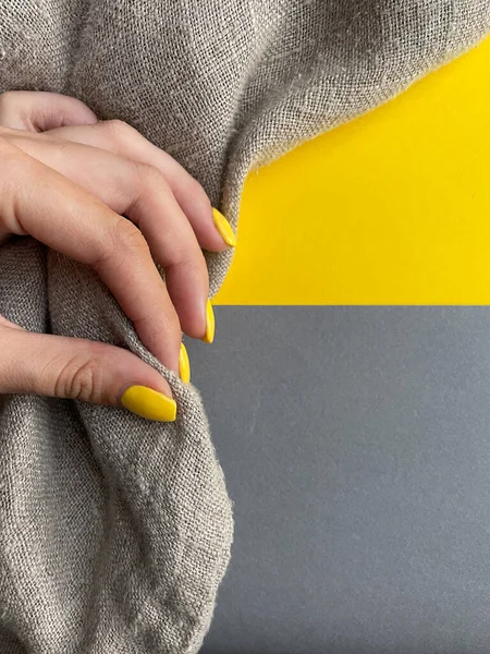 Kenevir kumaşı. Kumaşın dokusu. Gri arka plan. Sarı manikürlü bir kadın eli..