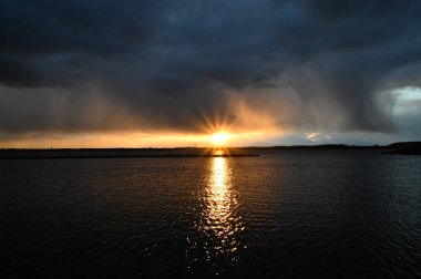 Rüzgarlı havalarda, dramatik bulutlarla gölün kıyısında güzel bir gün batımı..