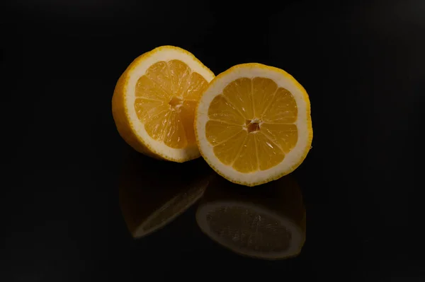 Close-up of a lemon cut in half with reflection on an isolated black background.