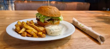 Bir kafede tabakta, patates kızartması ve bitki sosuyla servis edilen el yapımı peynirli burger..