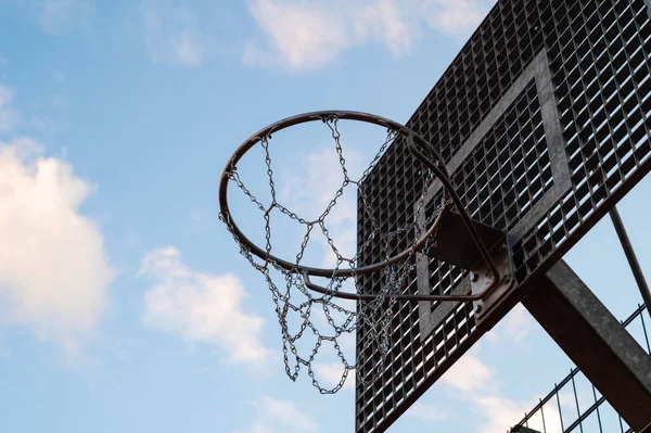 Outdoor metalic street basketball hoop with a blue sky in background.